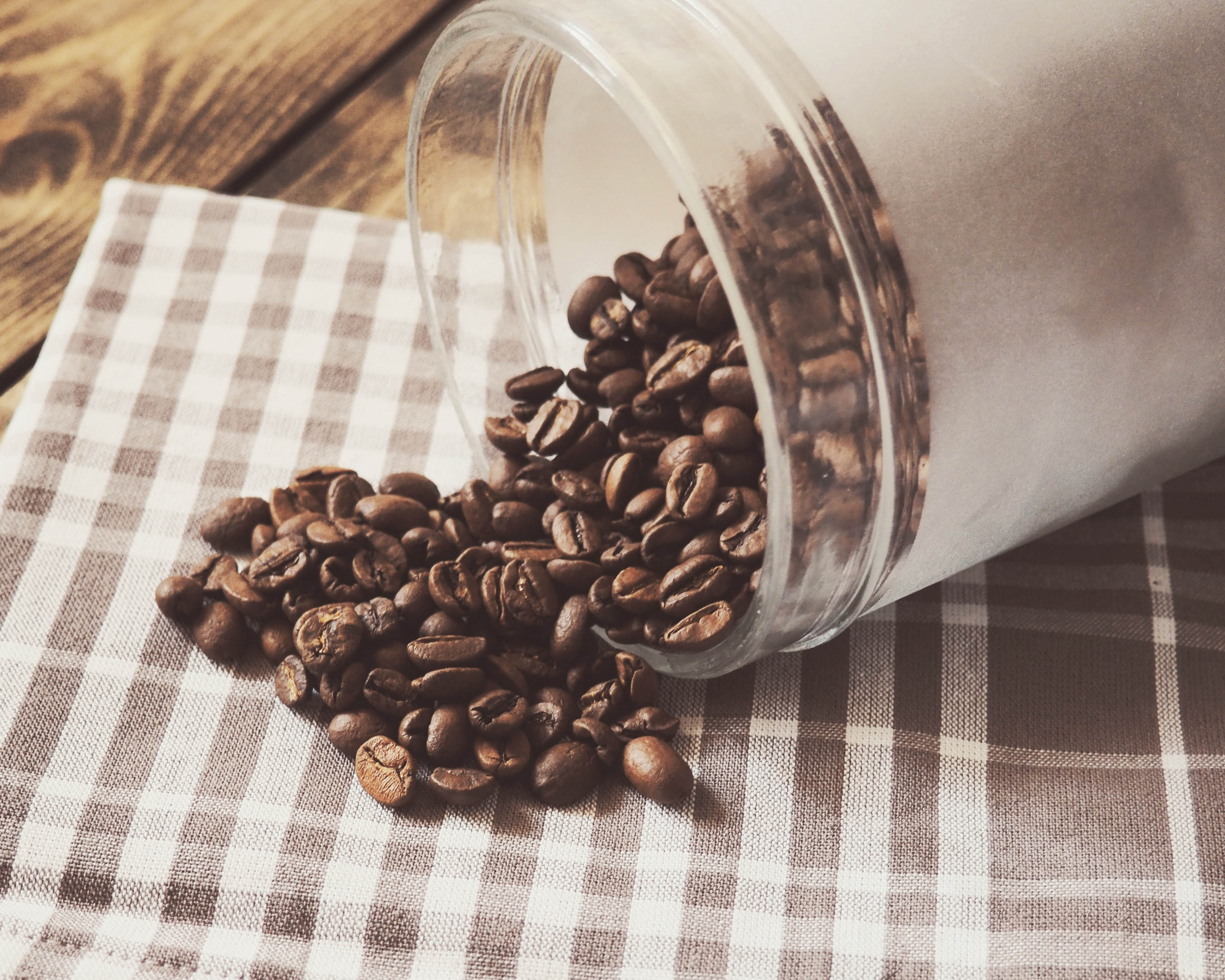 A photograph of a jar with coffee beans spilling out of it on top of a checkered cloth.